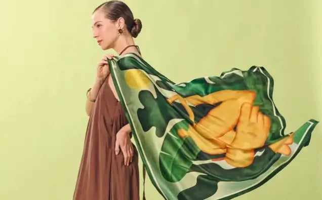 Imagem de modelo contra fundo verde com vestido marrom segurando o lenço Abaporu.