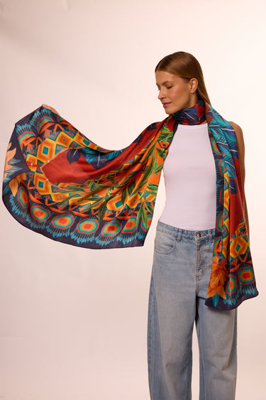 Mulher com cabelos castanhos claros usando lenço no pescoço colorido com padrão vibrante, roupa casual e fundo neutro. A imagem destaca a elegância e estilo com acessórios de moda.