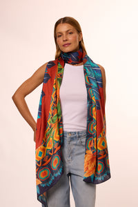 Mulher com cabelo castanho, usando camiseta branca e lenço no pescoço colorido com estampas vibrantes, posando com confiança contra fundo neutro.