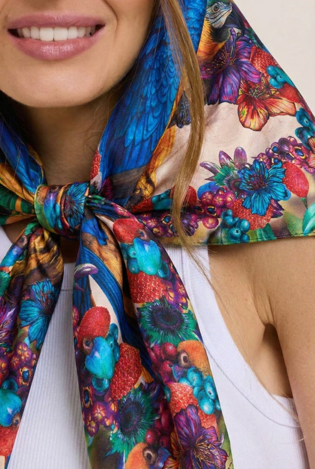 Imagem de modelo sorrindo, usando o lenço arara azul colorido com estampa de flores, pássaros e frutas, destacando o sorriso e o acessório vibrante.