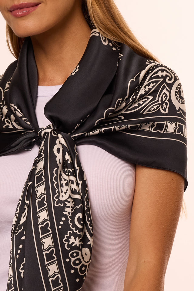 Mulher com lenço no pescoço preto com detalhes brancos e blusa branca, foco na parte superior do corpo, estilo casual e elegante