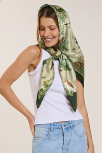 Mulher usando lenço de seda com estampa de natureza e animais, vestindo camiseta branca e jeans, sorrindo e com olhos fechados.