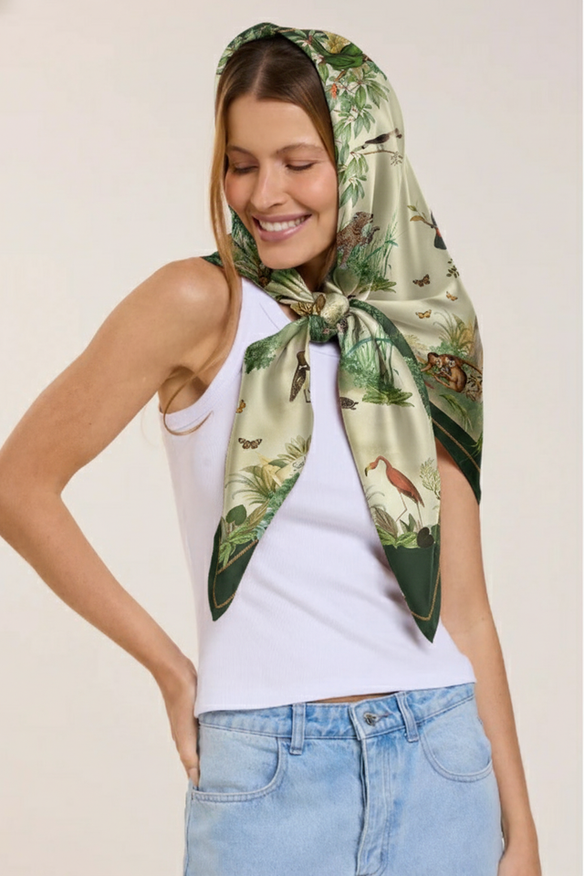 Mulher usando lenço de seda com estampa de natureza e animais, vestindo camiseta branca e jeans, sorrindo e com olhos fechados.