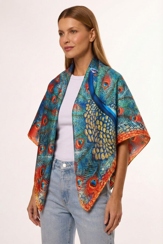 Mulher com cabelo castanho claro, vestindo blusa branca e lenço de seda com estampa de pavão em tons vibrantes de azul, verde, amarelo, e laranja, posando com sorriso suave sobre fundo branco.