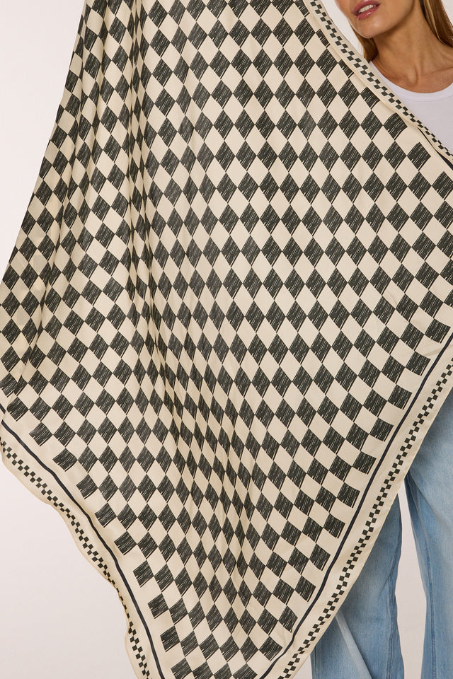 Lenço de seda Race com estampa xadrez em preto e branco, apresentado por modelo com blusa branca e jeans.