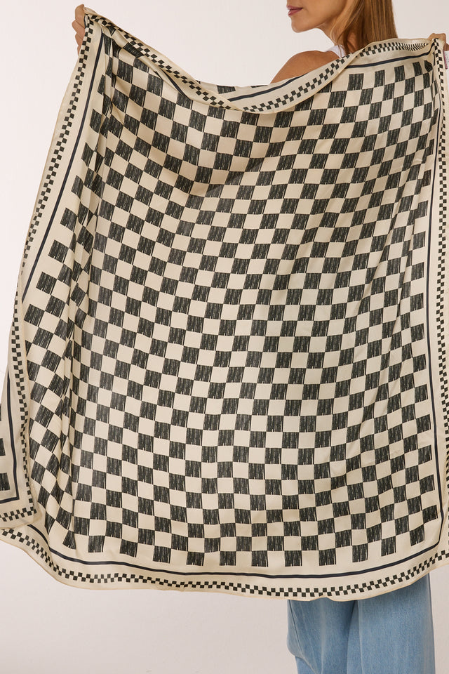 Mulher segurando lenço Race com padrão quadriculado preto e branco, com acabamento em borda decorativa, contra fundo branco.