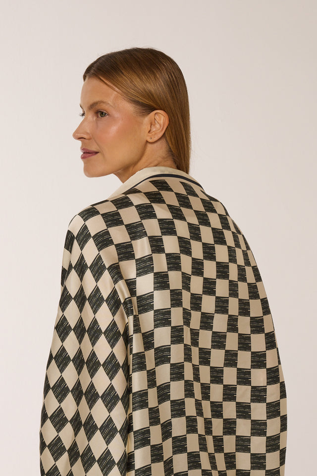 Mulher com cabelo castanho claro penteado para trás, usando o lanço Race quadriculado nos ombros, posando de perfil contra fundo branco.