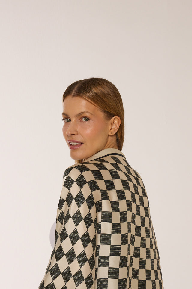 Mulher com cabelo castanho, rosto sorridente, vestindo lenço Race com estampa quadriculada em tom preto e branco e fundo branco.