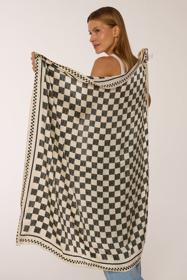 Modelo segurando o lenço Race preto e branco com padrão xadrez. Lenço para pescoço, blusa, acessório e mais. A mulher posa de perfil contra fundo claro.