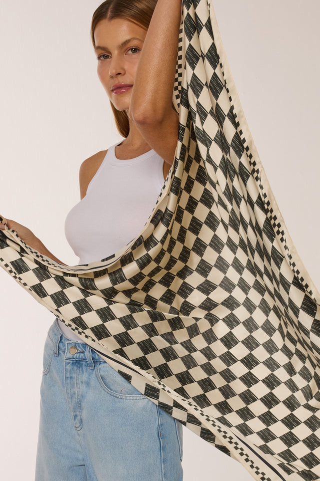 Mulher com cabelo castanho, vestindo regata branca e jeans, segurando o lenço Race, pose elegante.