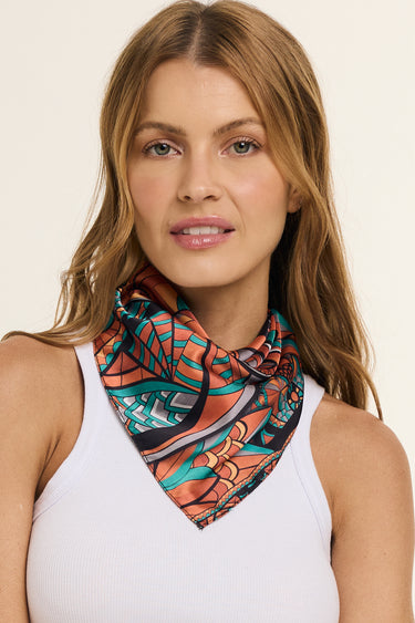 Mulher vestindo lenço no pescoço Lobo Guará do Cerrado, em cetim de poliéster. O modelo possui tons em verde, laranja, preto e cinza.