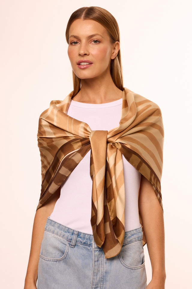 Modelo vestindo lenço de seda em tons de bege, dourado e marrom, com cabelo liso e looks casuais e elegantes.