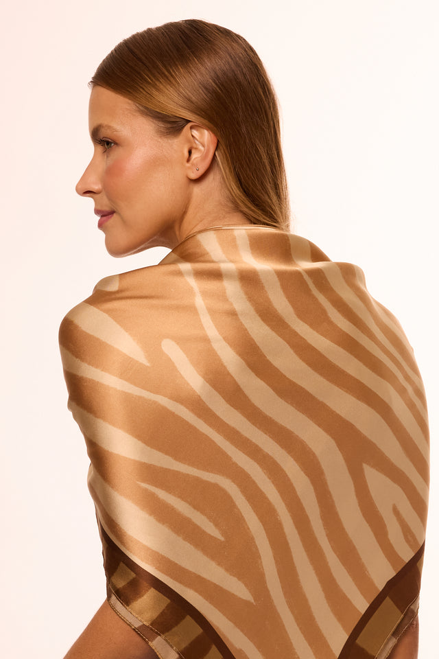 Mulher com cabelo castanho claro, vista de costas, usando lenço de seda com estampa de zebra ou tigre em tons de bege, dourado e marrom, olhando de perfil.
